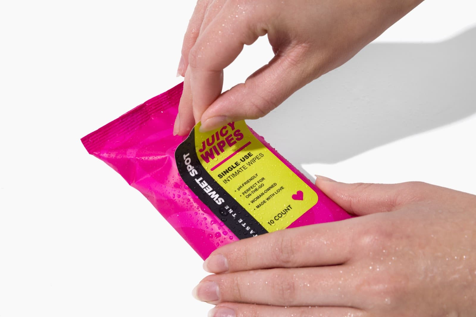 Hands opening a pink pack of Juicy Wipes