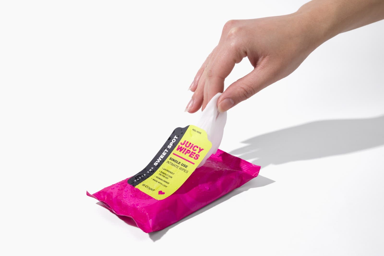 A hand pulls one wipe from a pink Juicy Wipes pack