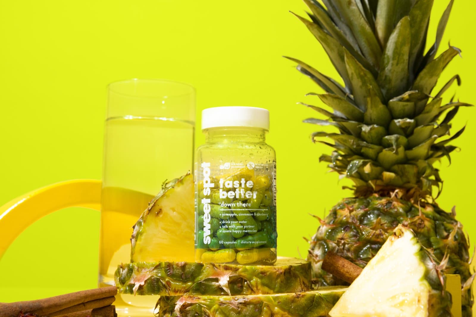 For Him bottle in front of pineapple slices, a glass of water, and a whole pineapple