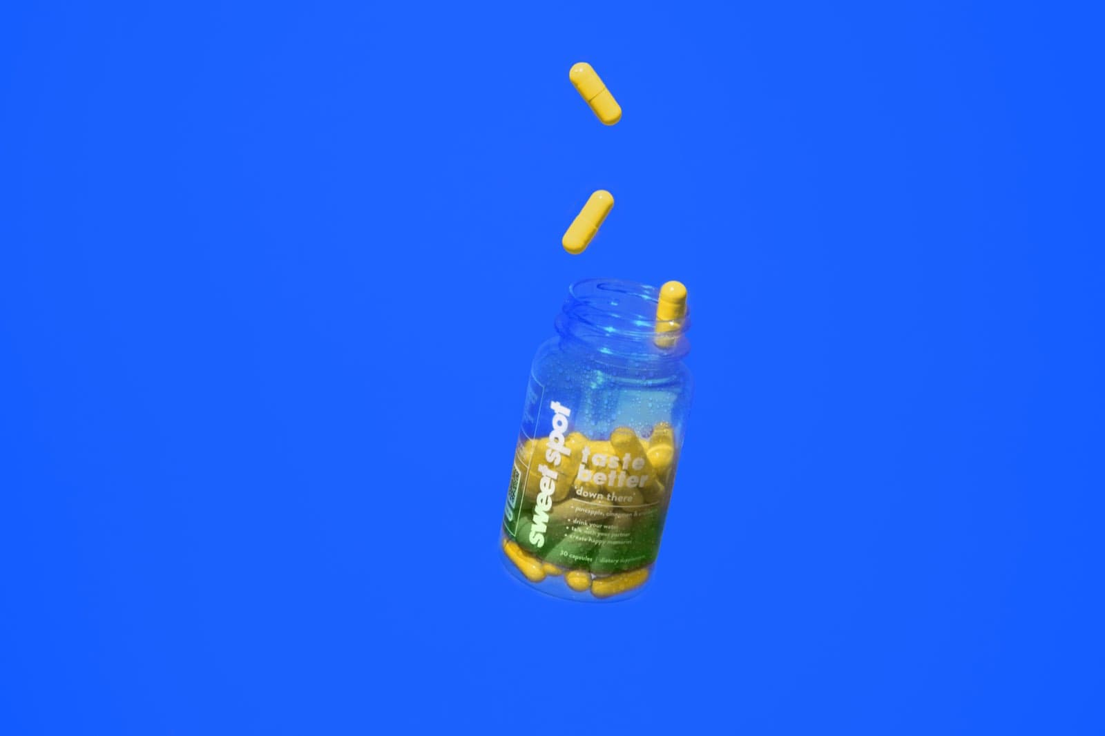 Yellow capsules falling toward an open For Him bottle against blue