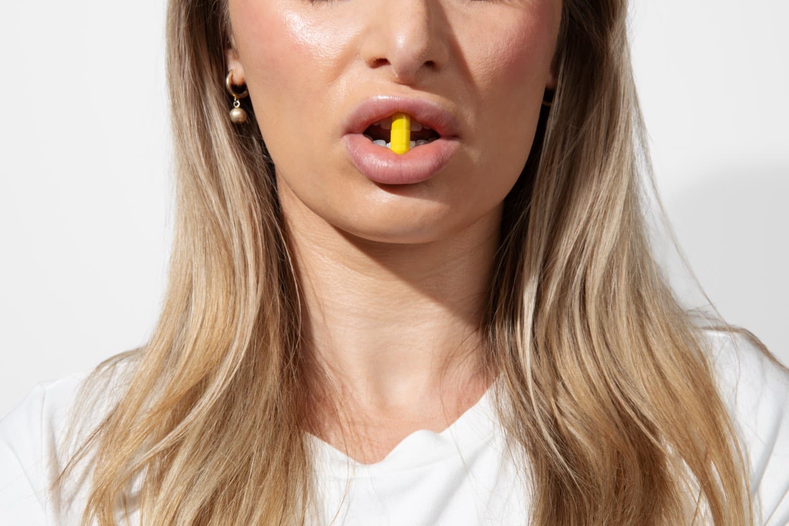 Close portrait of a woman with a yellow capsule between her lips