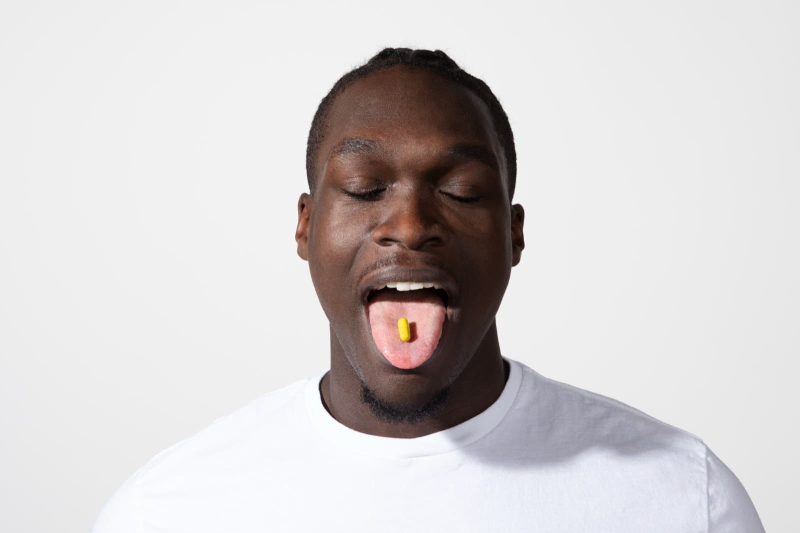 A man with his eyes closed and a yellow capsule on his tongue