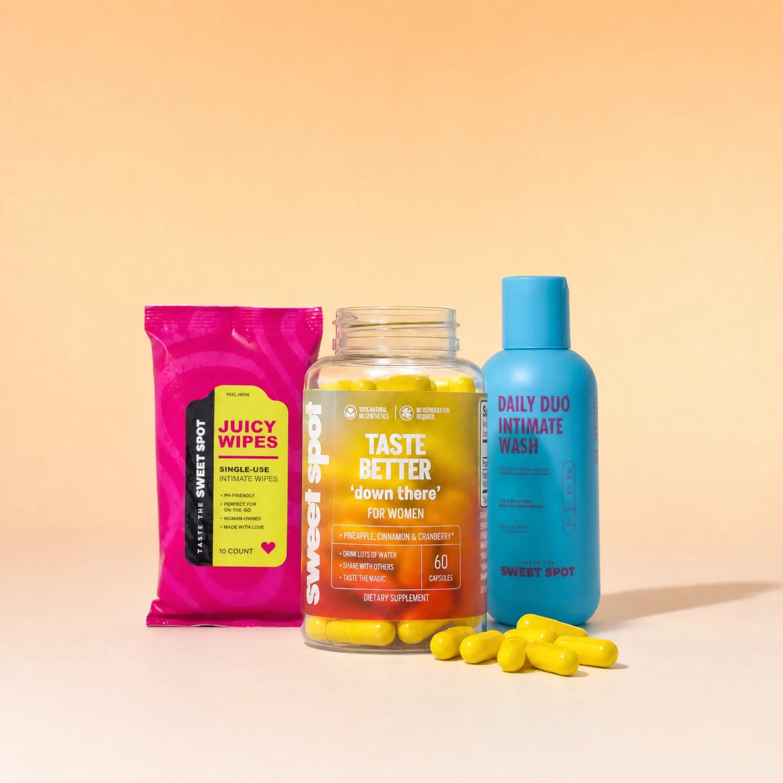 A pink Juicy Wipes packet, an open taste better down there for women bottle, and a blue Daily Duo Intimate Wash sit with loose yellow capsules.