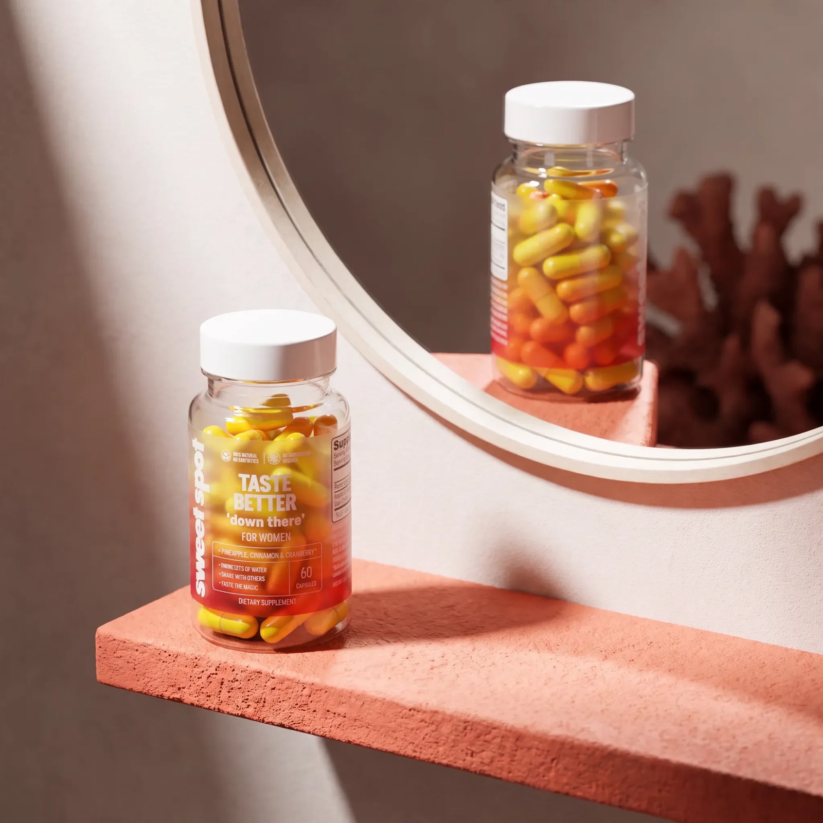 A Taste Better down there For Women bottle of yellow and orange capsules sits on a coral shelf, reflected in a round mirror.