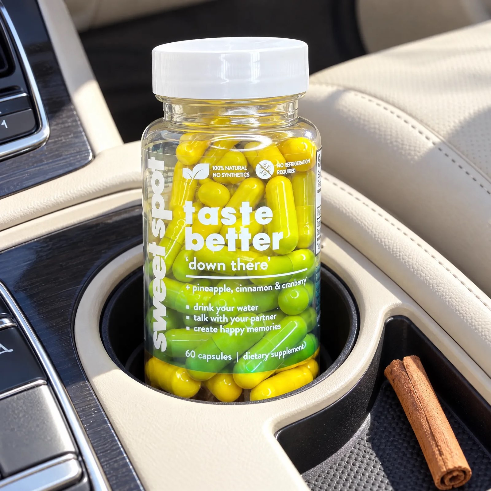 A green and yellow capsule bottle labeled taste better down there and sweet spot sits in a car cup holder beside a cinnamon stick.