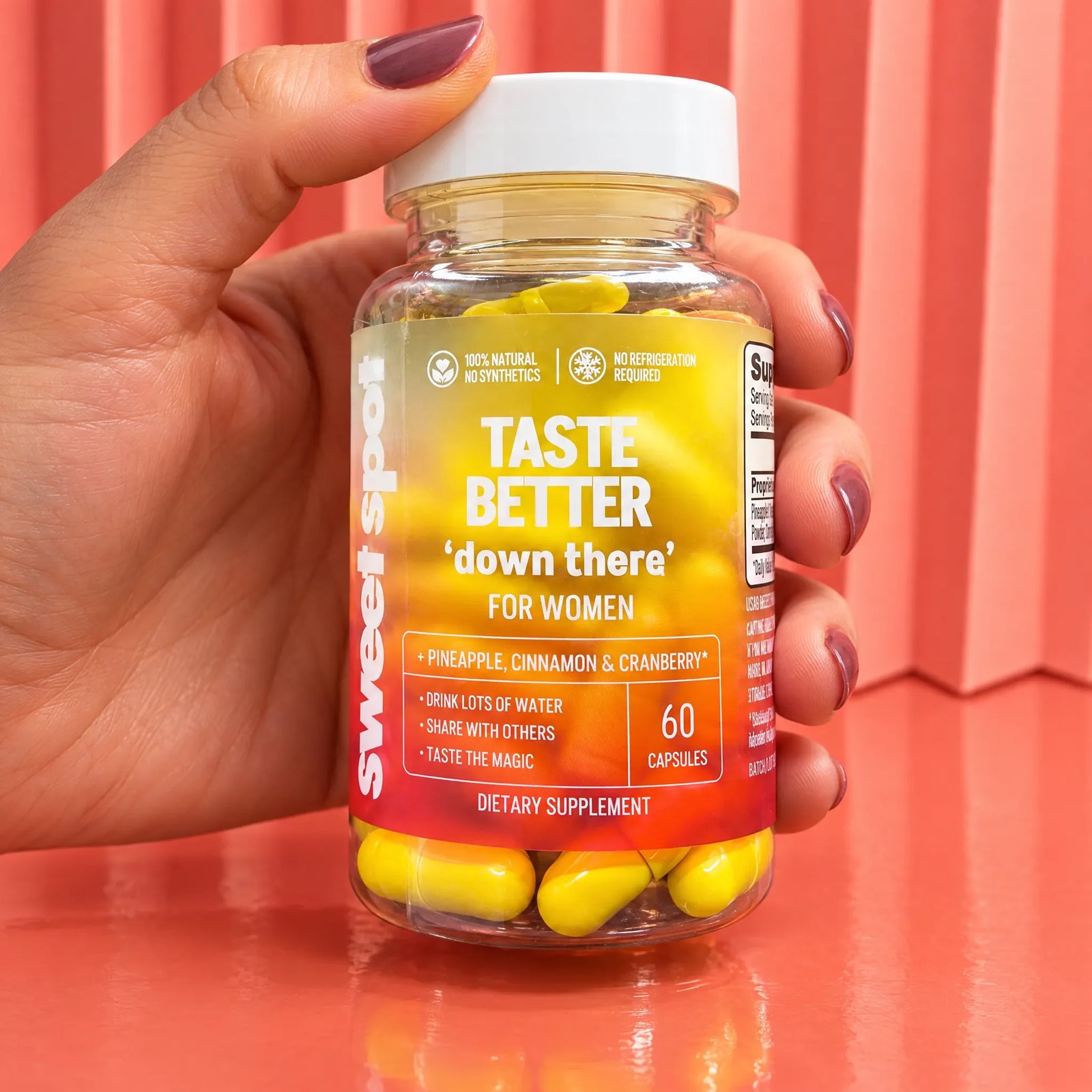 A hand with mauve nails holds a Taste Better down there For Women bottle of yellow capsules against a coral pleated background.