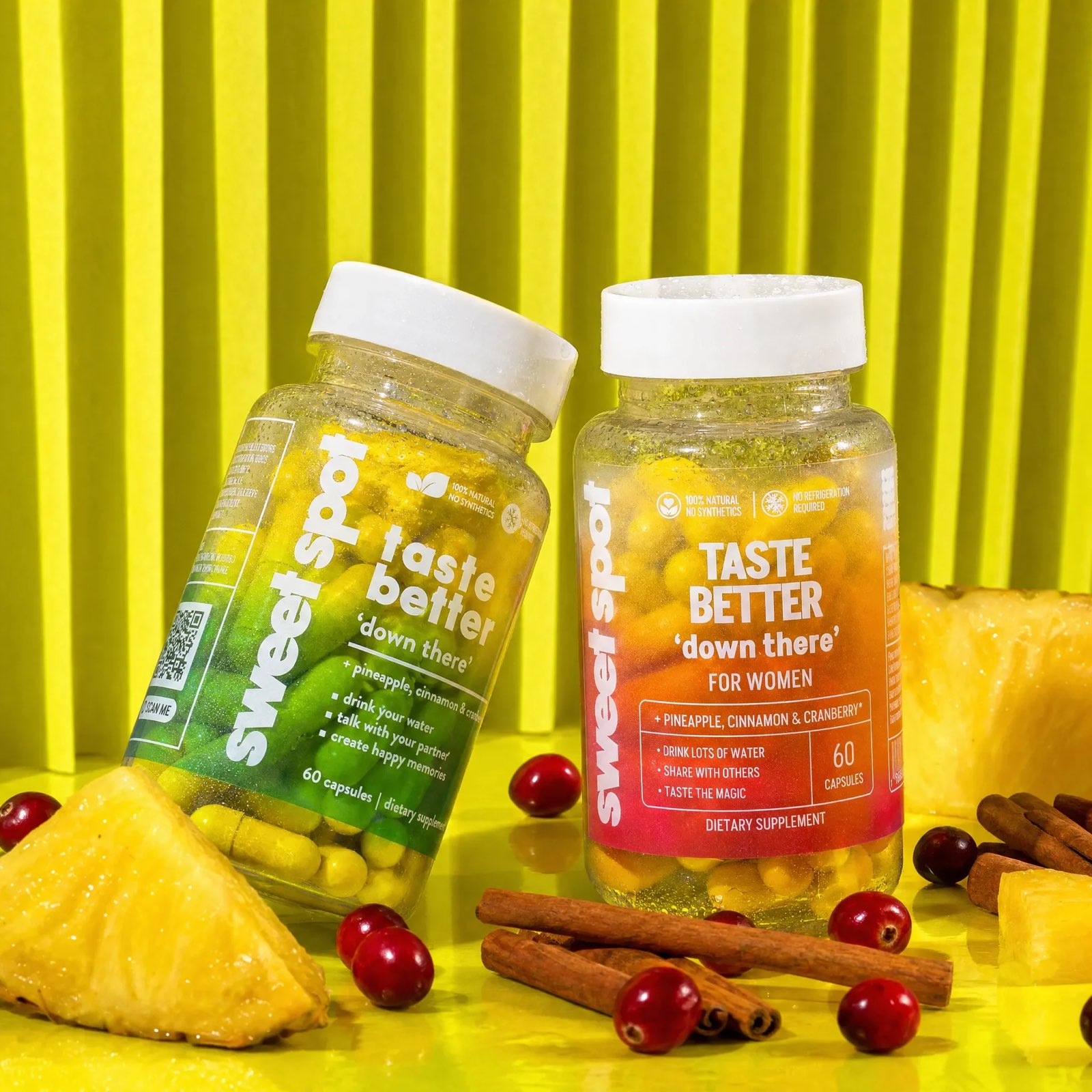 A green taste better down there bottle and an orange For Women bottle lean on yellow with pineapple wedges, cranberries, and cinnamon sticks.