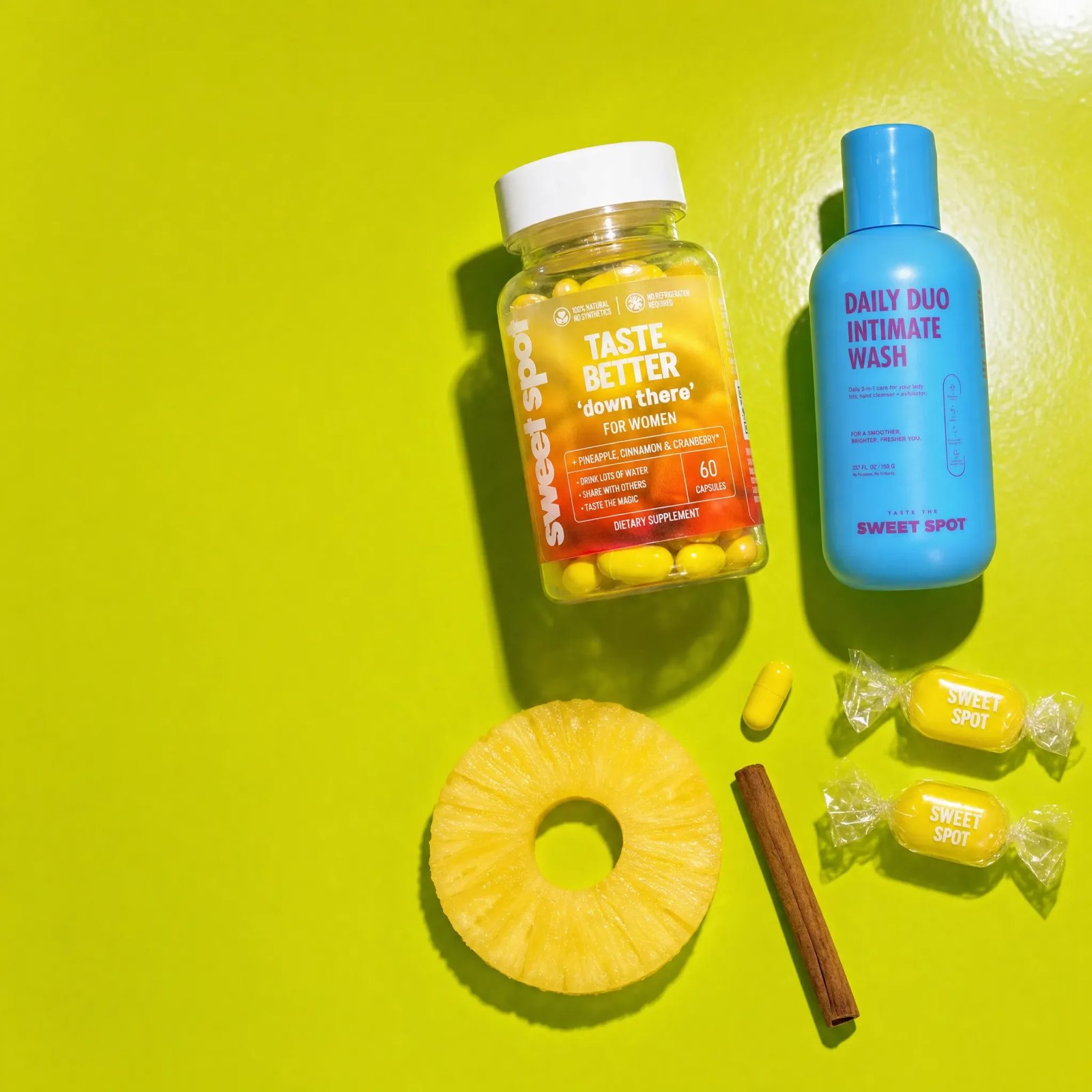 On a lime surface, a Taste Better down there for women bottle sits beside a blue Daily Duo Intimate Wash, a pineapple ring, cinnamon, and yellow candies.
