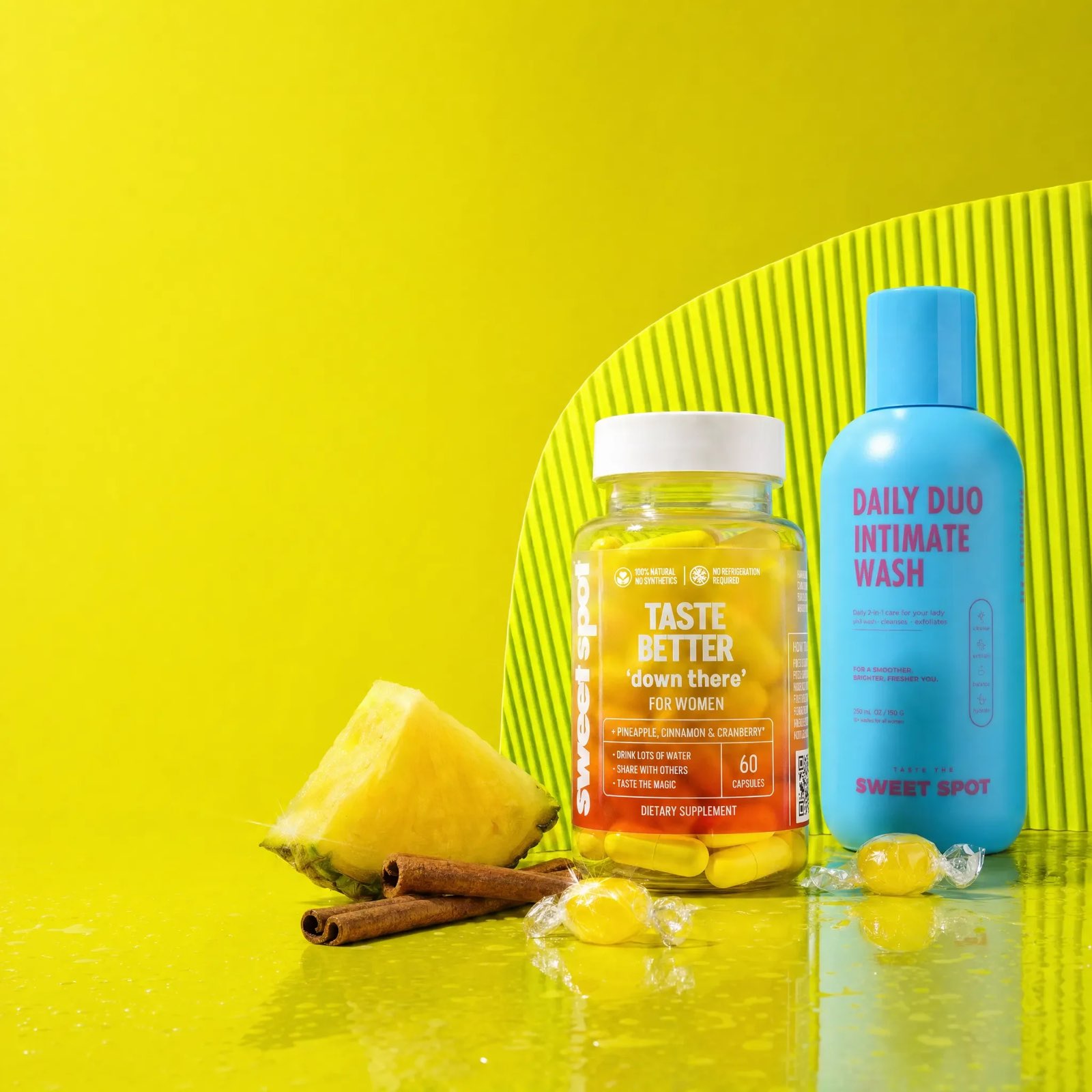 A pineapple wedge and cinnamon sticks sit with a Taste Better down there for women bottle and a blue Daily Duo Intimate Wash on a lime surface.