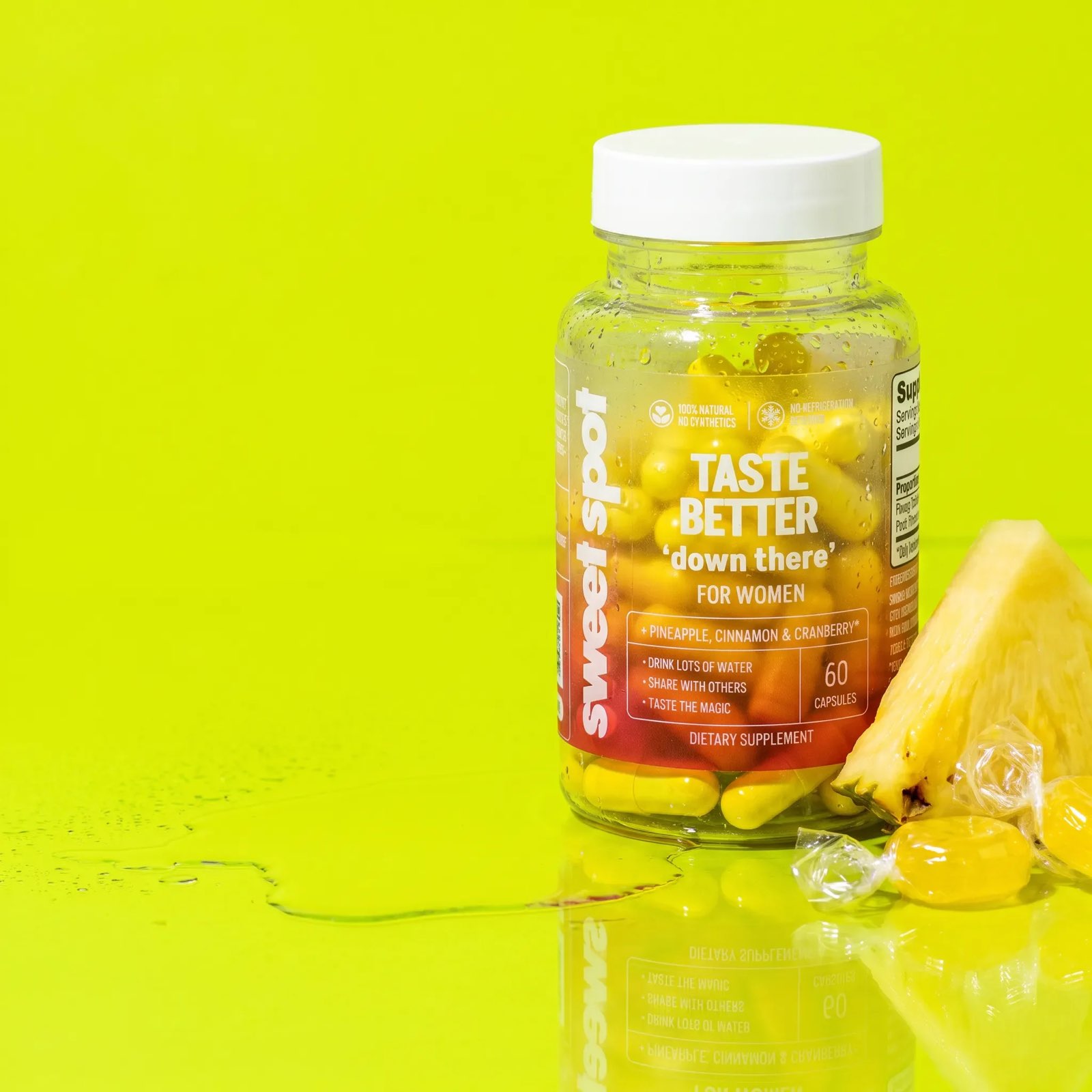 A wet Taste Better down there for women bottle stands on a lime surface beside a pineapple wedge and wrapped yellow capsules.