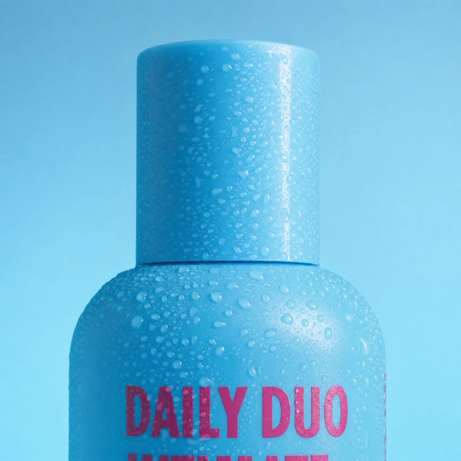 A close crop of a blue Daily Duo bottle shows water droplets across the cap and the pink Daily Duo lettering on the shoulder.