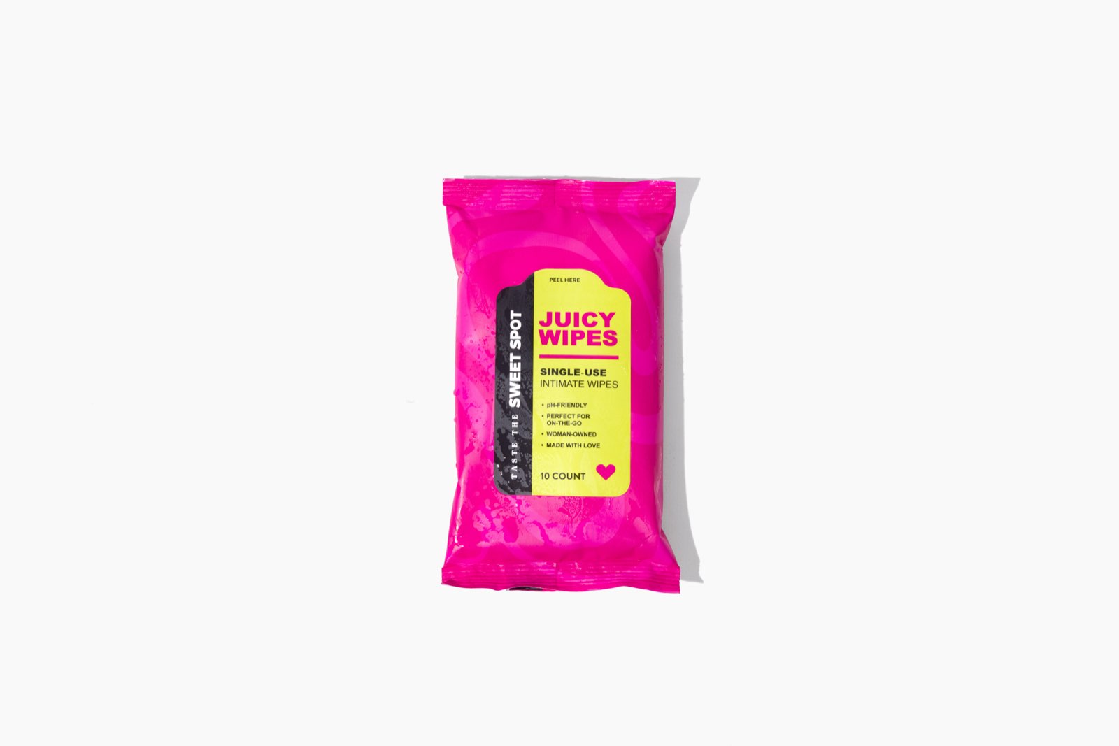 A pink Juicy Wipes packet sits centered on a wide white background, its yellow label reading single-use intimate wipes and Taste the Sweet Spot.