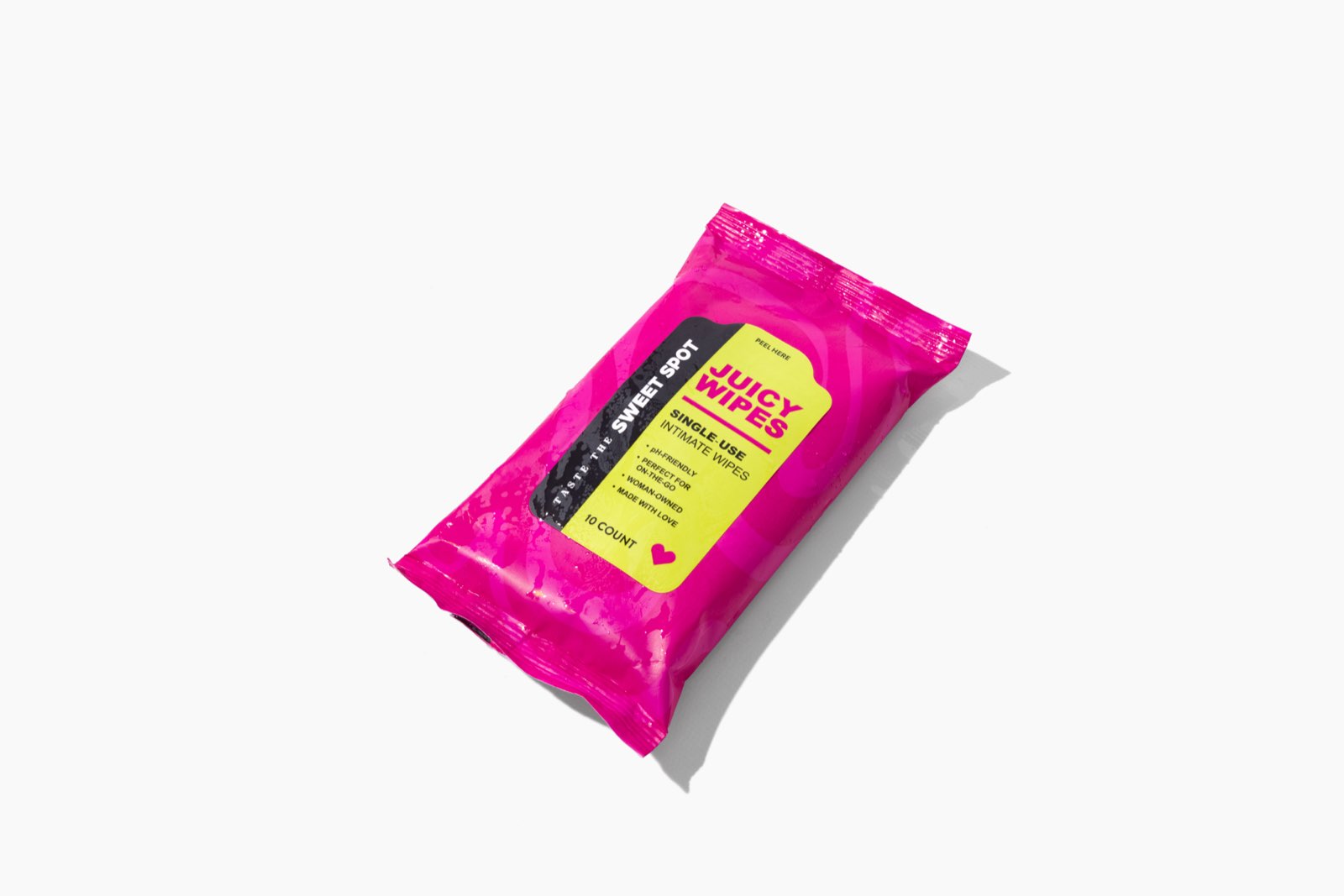 A pink Juicy Wipes packet rests at an angle on white, showing a yellow label that reads single-use intimate wipes and Taste the Sweet Spot.