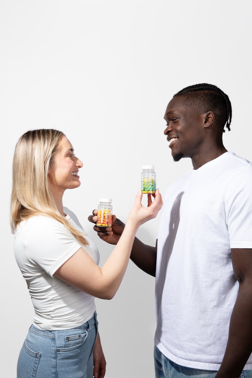 A blonde woman and a man in white shirts smile as she holds an orange taste better down there bottle and he holds a green Sweet Spot bottle.